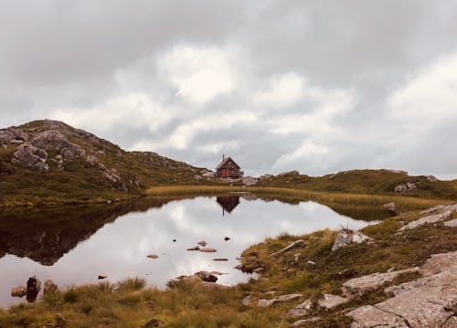 Cabin on Green Grass Field Near Lake Under White Clouds