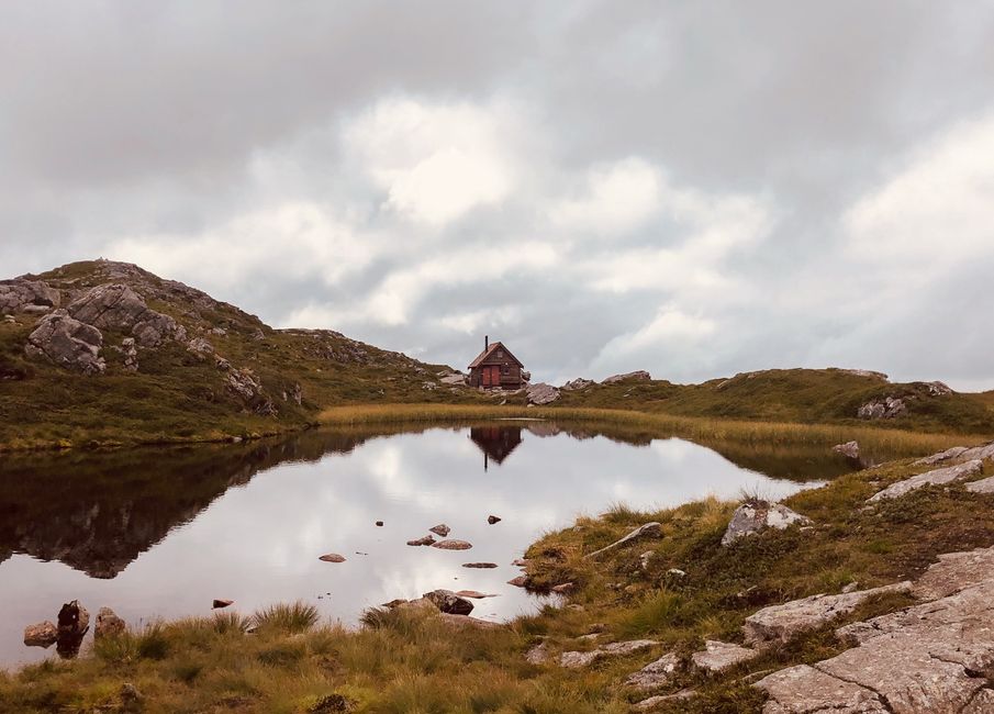 Serene mountain scene with a rustic cabin reflected in a lake near Bergen, Norway.