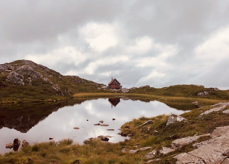 Cabin On Green Grass Field Near Lake Under White Clouds