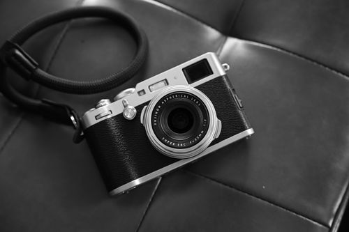 Free A stylish vintage camera with a lens and strap resting on a leather surface, captured in black and white. Stock Photo