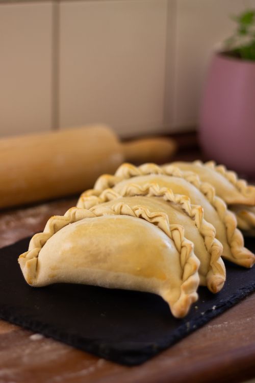 Free Freshly baked empanadas arranged on a slate board in a cozy kitchen setting. Stock Photo