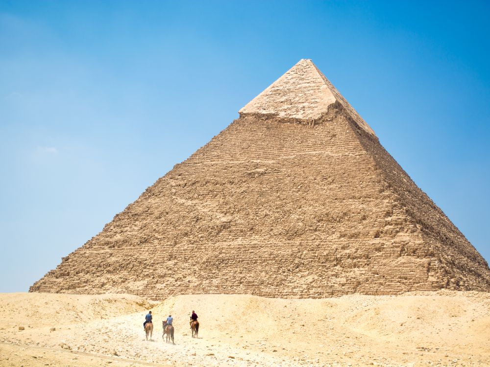 People riding a camel near pyramid under blue sky, Egypt