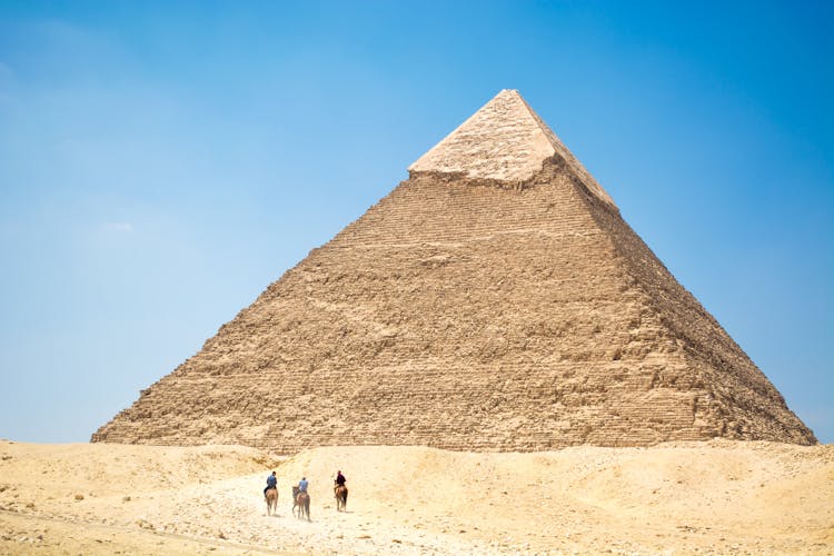 People Riding A Camel Near Pyramid Under Blue Sky