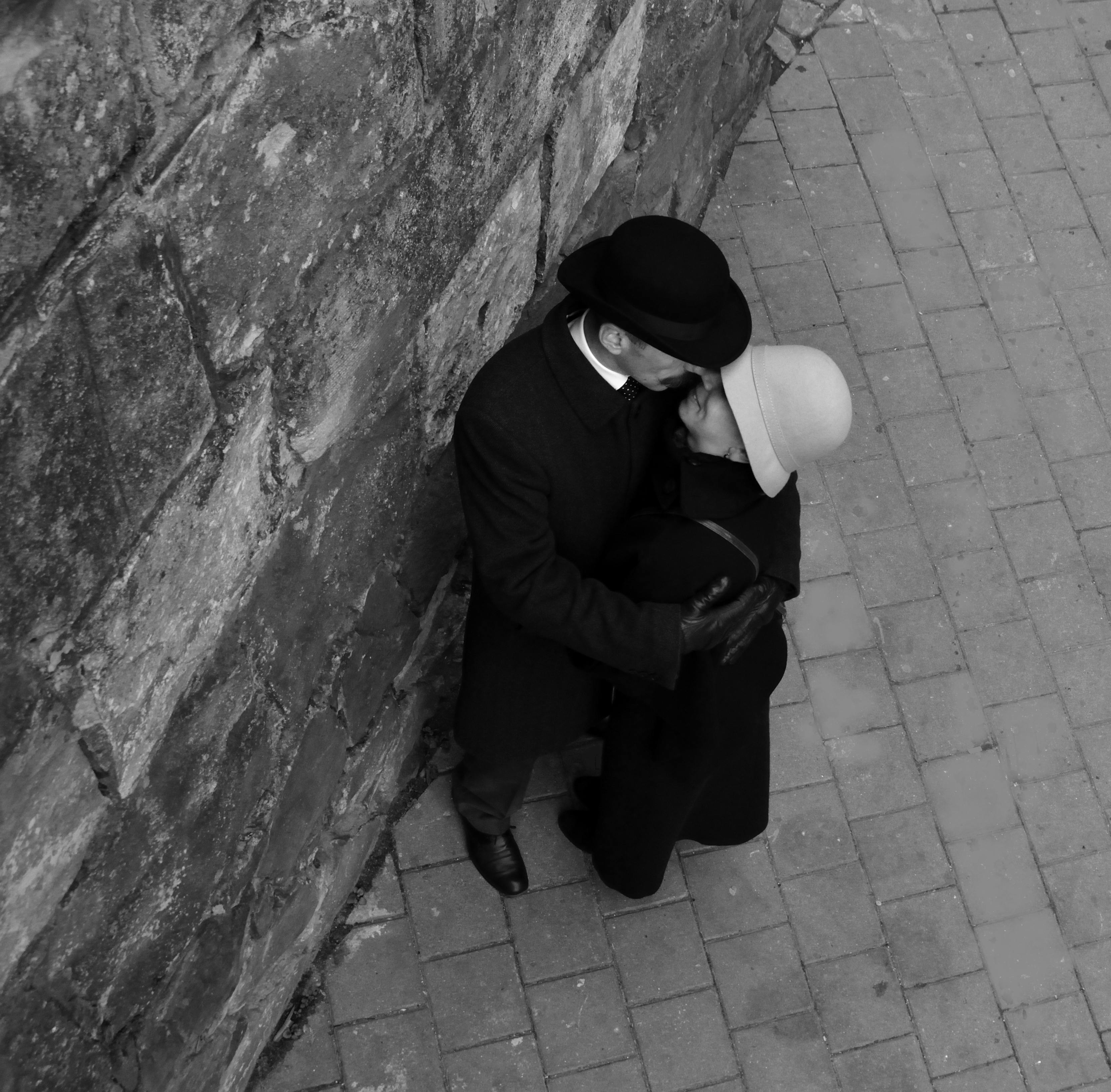 A couple embraces against a stone wall in Lviv, Ukraine, capturing love in monochrome.