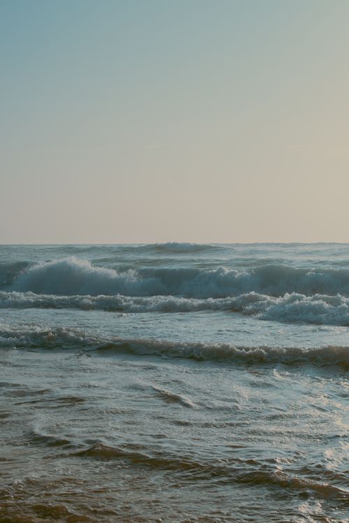 Free Peaceful ocean waves crashing with a warm sunrise in the background. Stock Photo