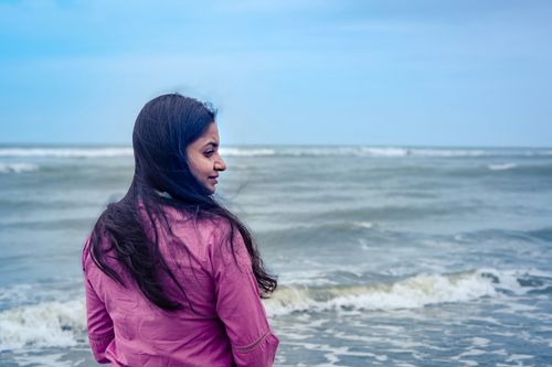 Free Woman in pink enjoying the serene ocean view on a breezy day. Stock Photo