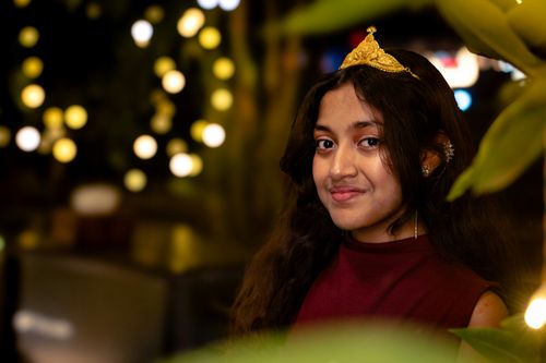 Free A teenager smiling while wearing a golden tiara, surrounded by lights at night. Stock Photo