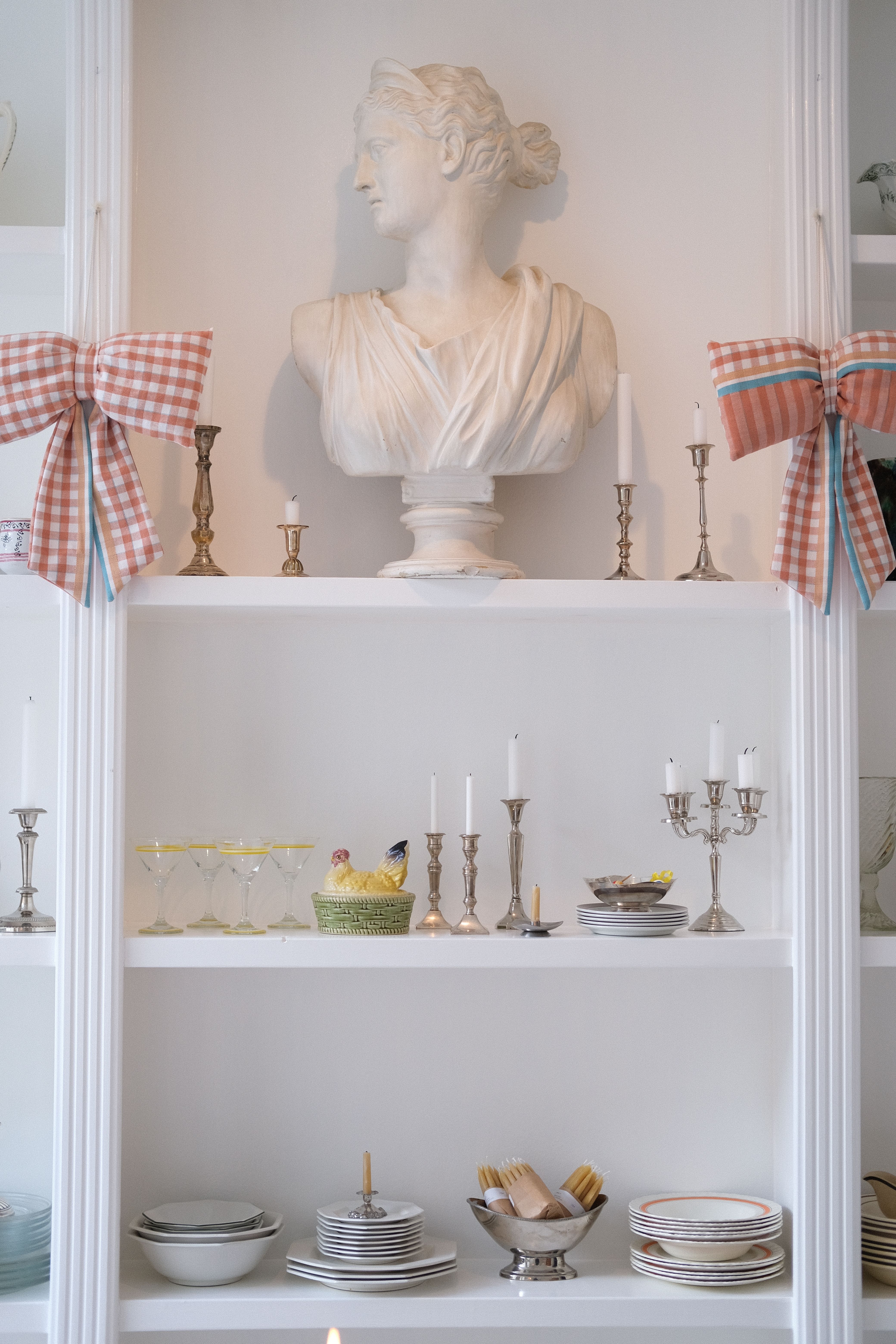 A harmonious shelf display featuring a classic ceramic bust, candlesticks, and neatly arranged crockery for a timeless decor.