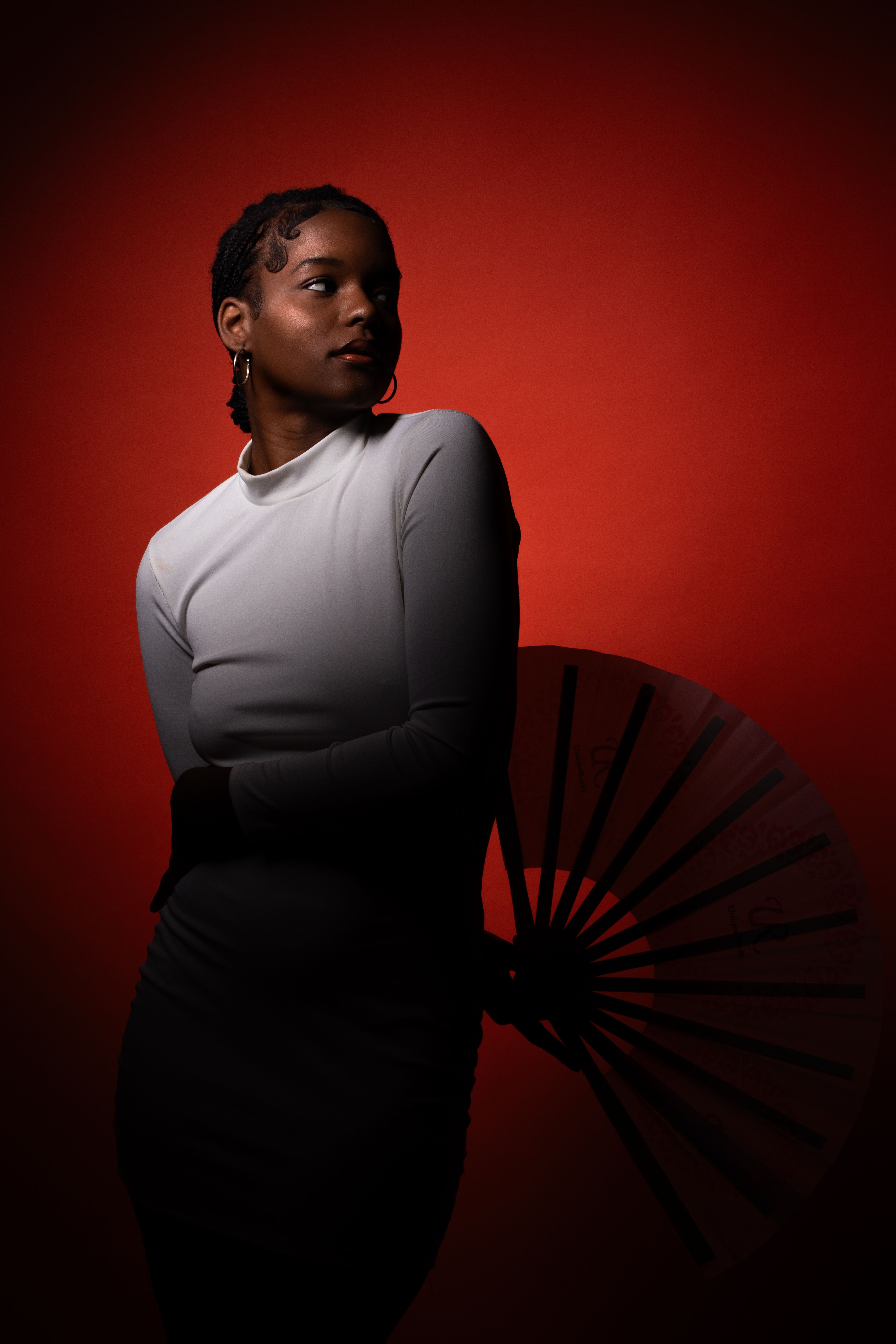 Elegant portrait of a woman in white against a striking red backdrop holding an umbrella. Artistic lighting.