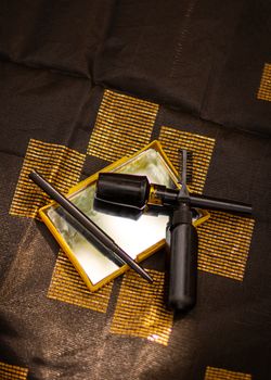 A stylish arrangement of black makeup tools on a patterned fabric background creating a dramatic aesthetic.