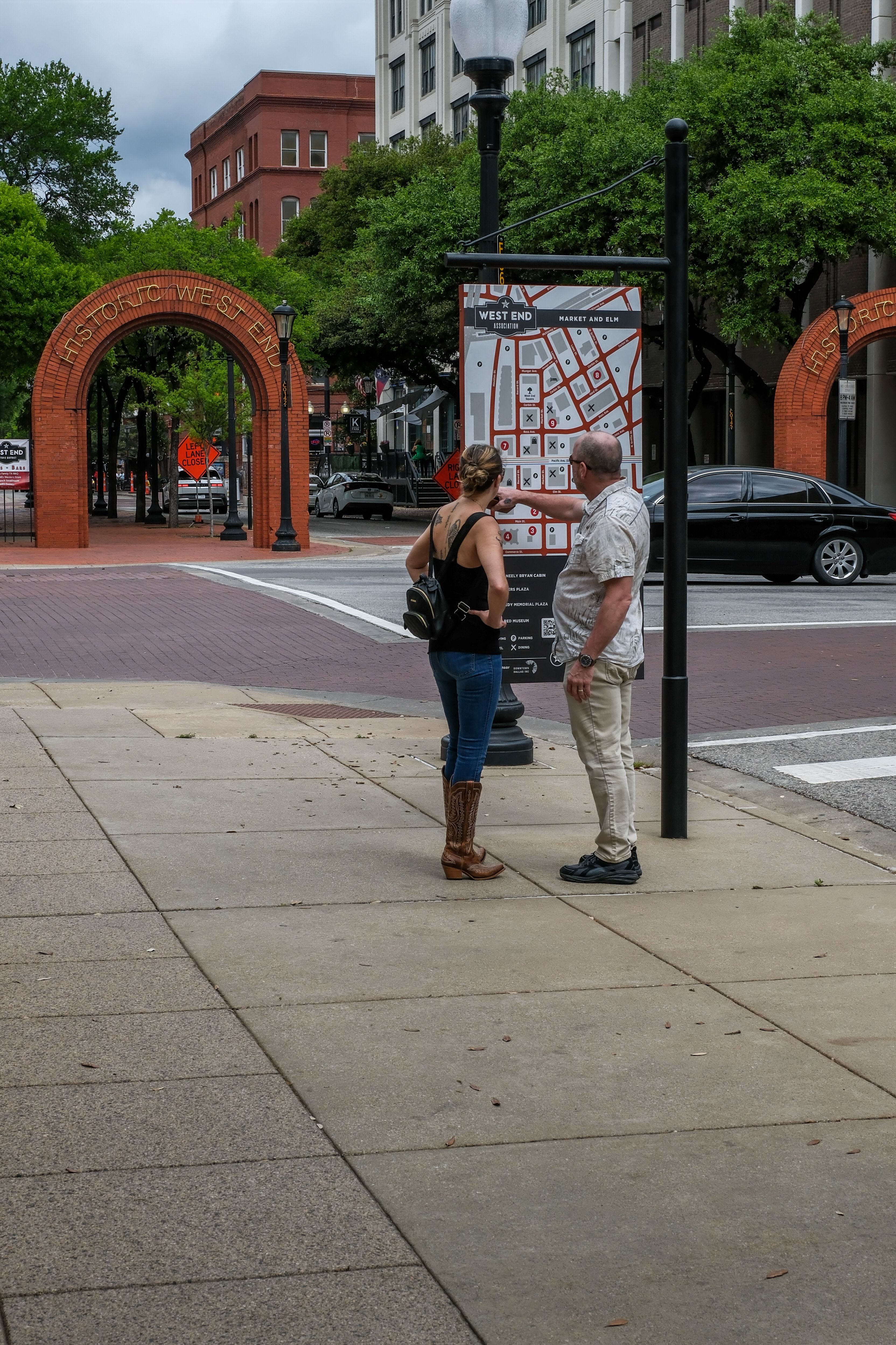 Tourists in the Historic West End of Dallas exploring the area map on a cloudy day - visitor bureau history trails