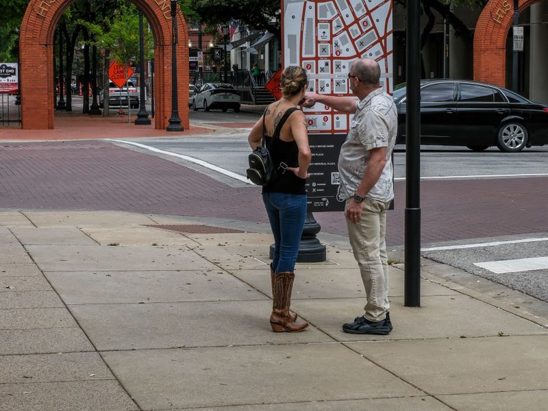 Tourists in the Historic West End of Dallas exploring the area map on a cloudy day - visitor bureau history trails