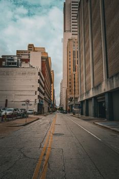 A quiet urban street flanked by towering skyscrapers on a cloudy day.