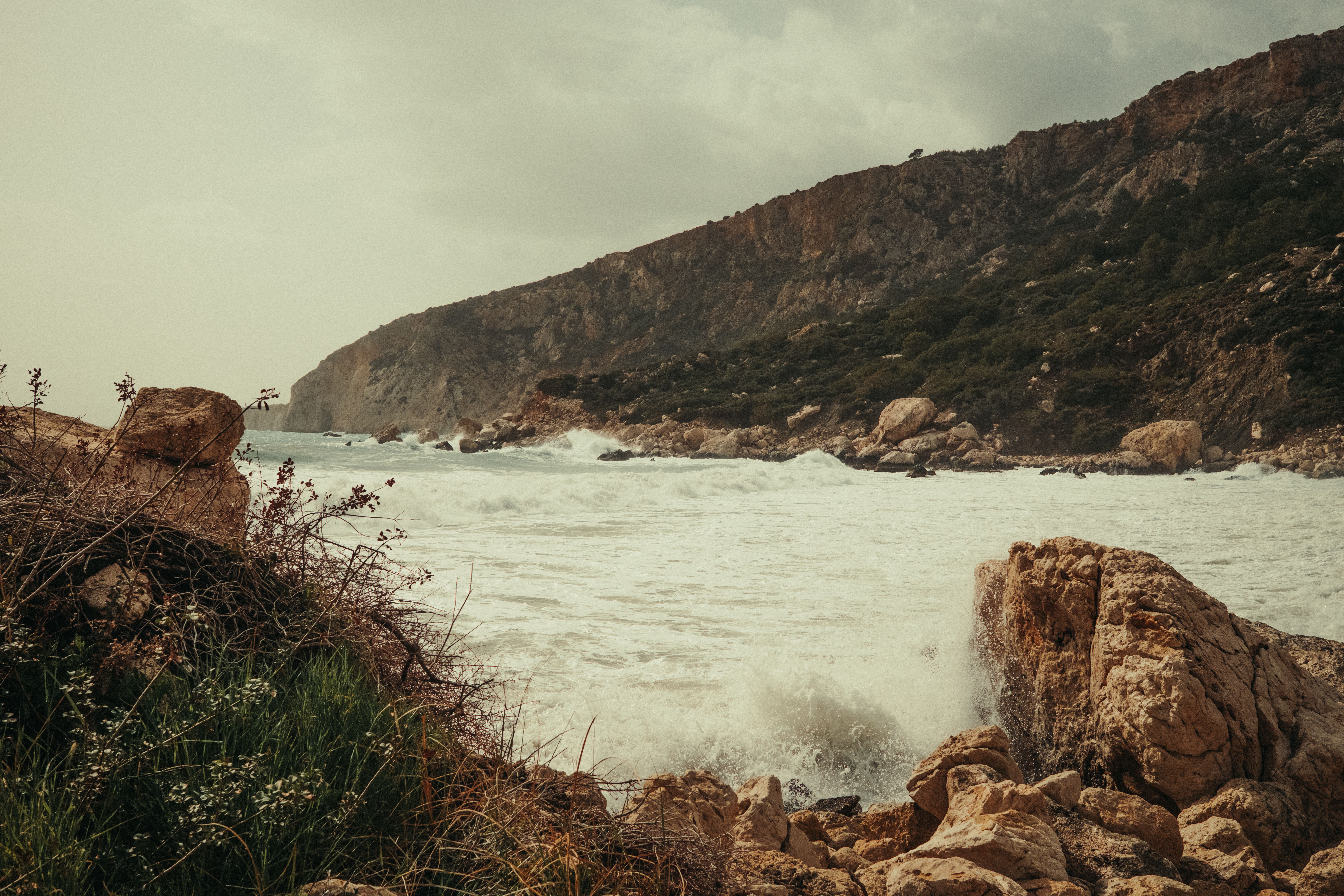 Waves crashing against rocky cliffs under a cloudy sky, showcasing dramatic seascape.