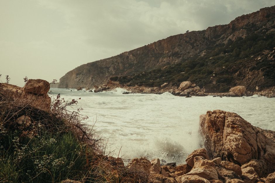 Waves crashing against rocky cliffs under a cloudy sky, showcasing dramatic seascape.