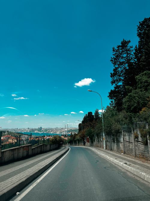 Free A picturesque curved road leading toward a distant city skyline under a vibrant blue sky. Stock Photo