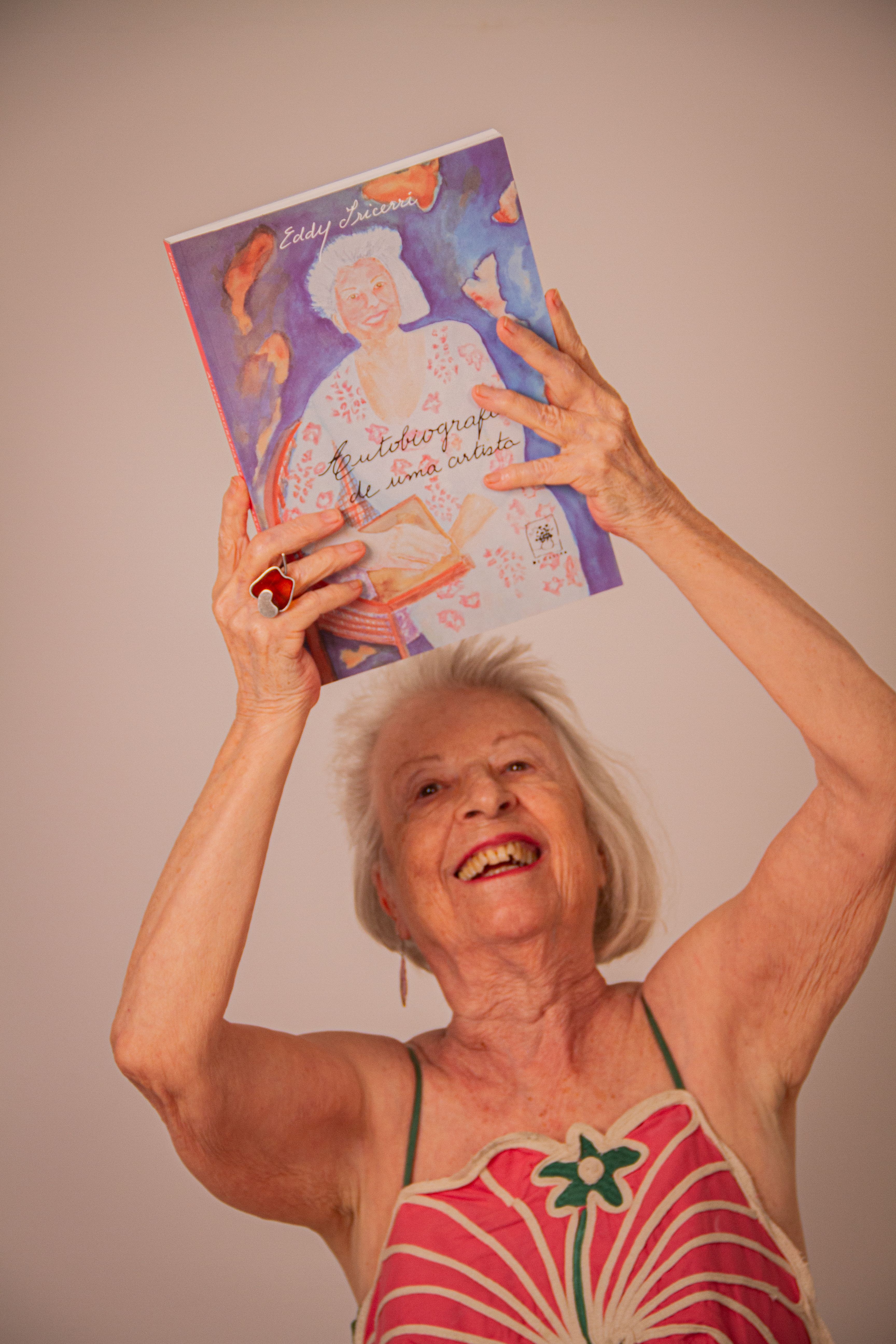 Happy senior woman joyfully holding a colorful book above her head.