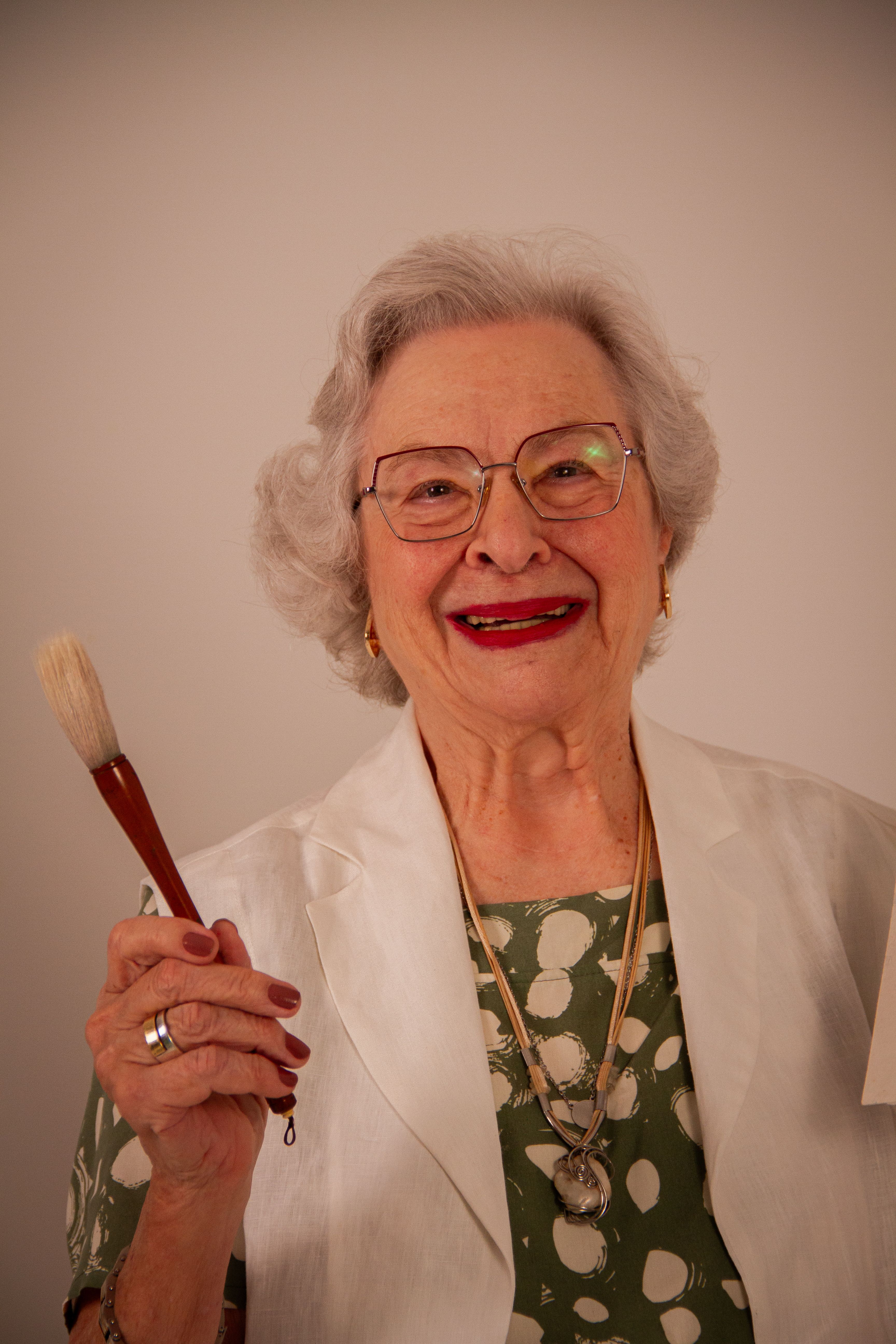 Charming elderly woman smiling with a paintbrush, showcasing artistic enthusiasm indoors.