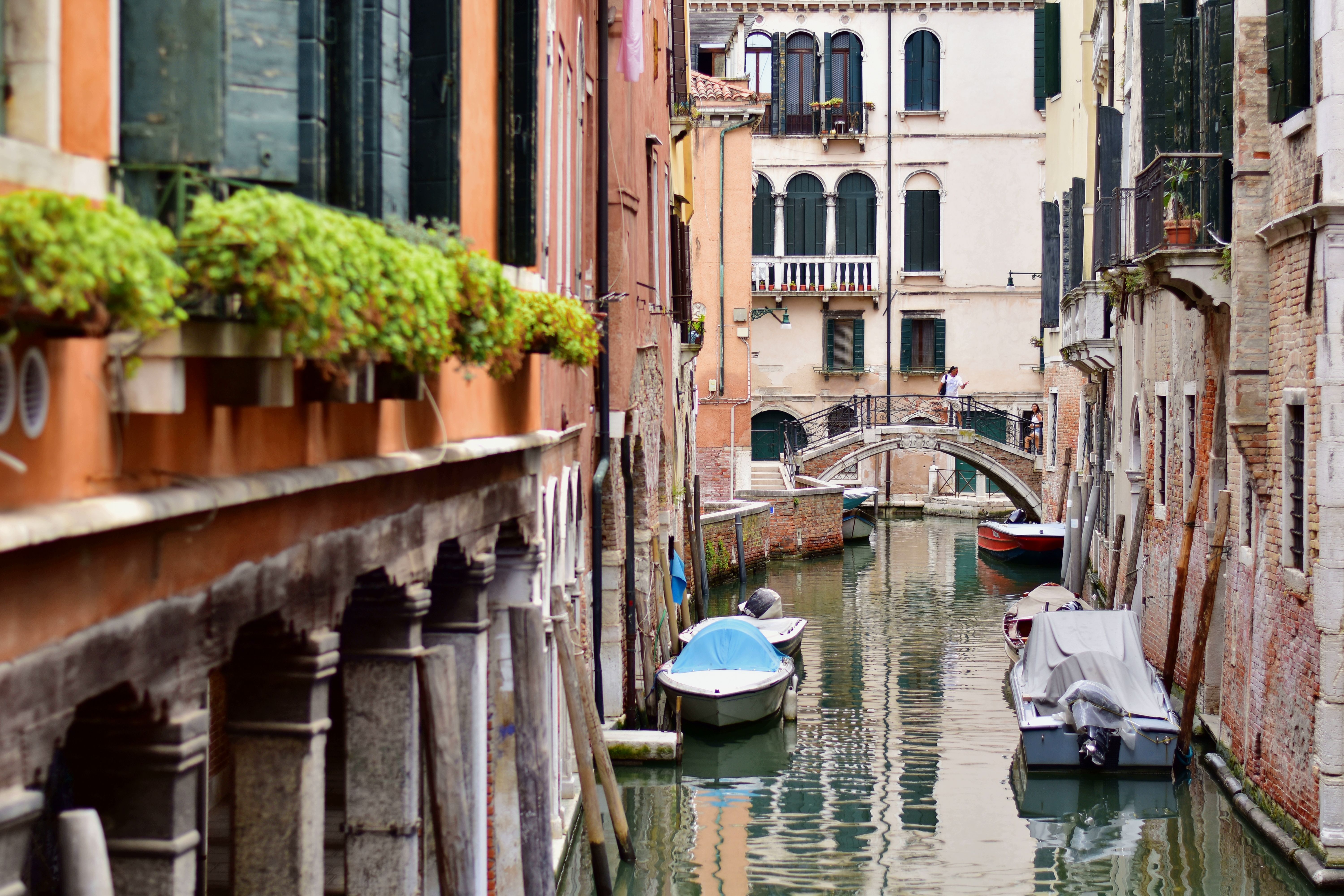Charming view of a narrow Venetian canal lined with boats and a quaint bridge under summer's light.