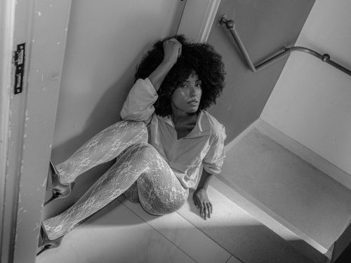 Free Artistic black and white portrait of a woman sitting in a stairwell, wearing lace tights and a relaxed shirt. Stock Photo