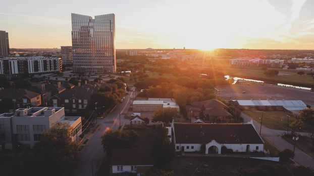 Aerial view of a cityscape with tall modern buildings and sunset in the background.