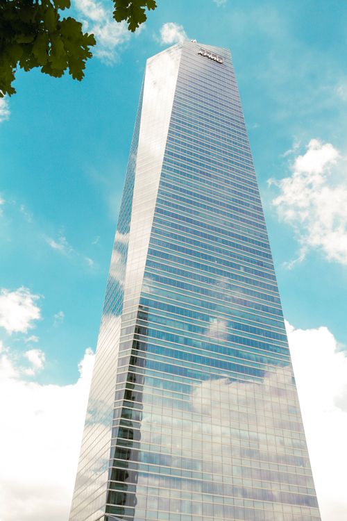 Free Tall glass skyscraper reflecting clouds with clear blue sky background. Stock Photo