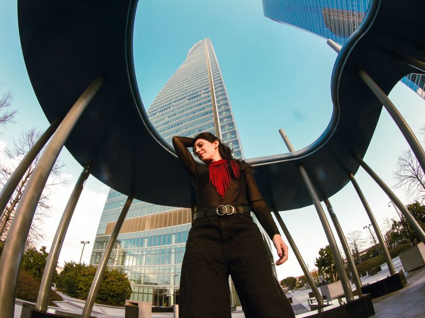 Stylish woman poses confidently in a modern Madrid urban environment with skyscrapers.