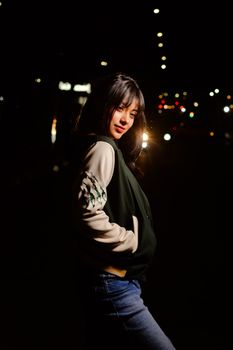 Stylish young woman posing at night on a city street, illuminated by streetlights.