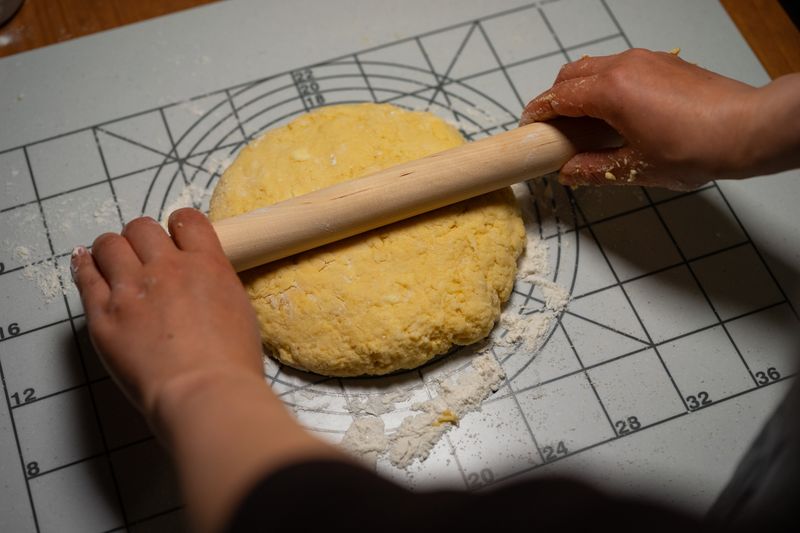 Close-up of hands using a rolling pin to flatten dough on a baking mat.