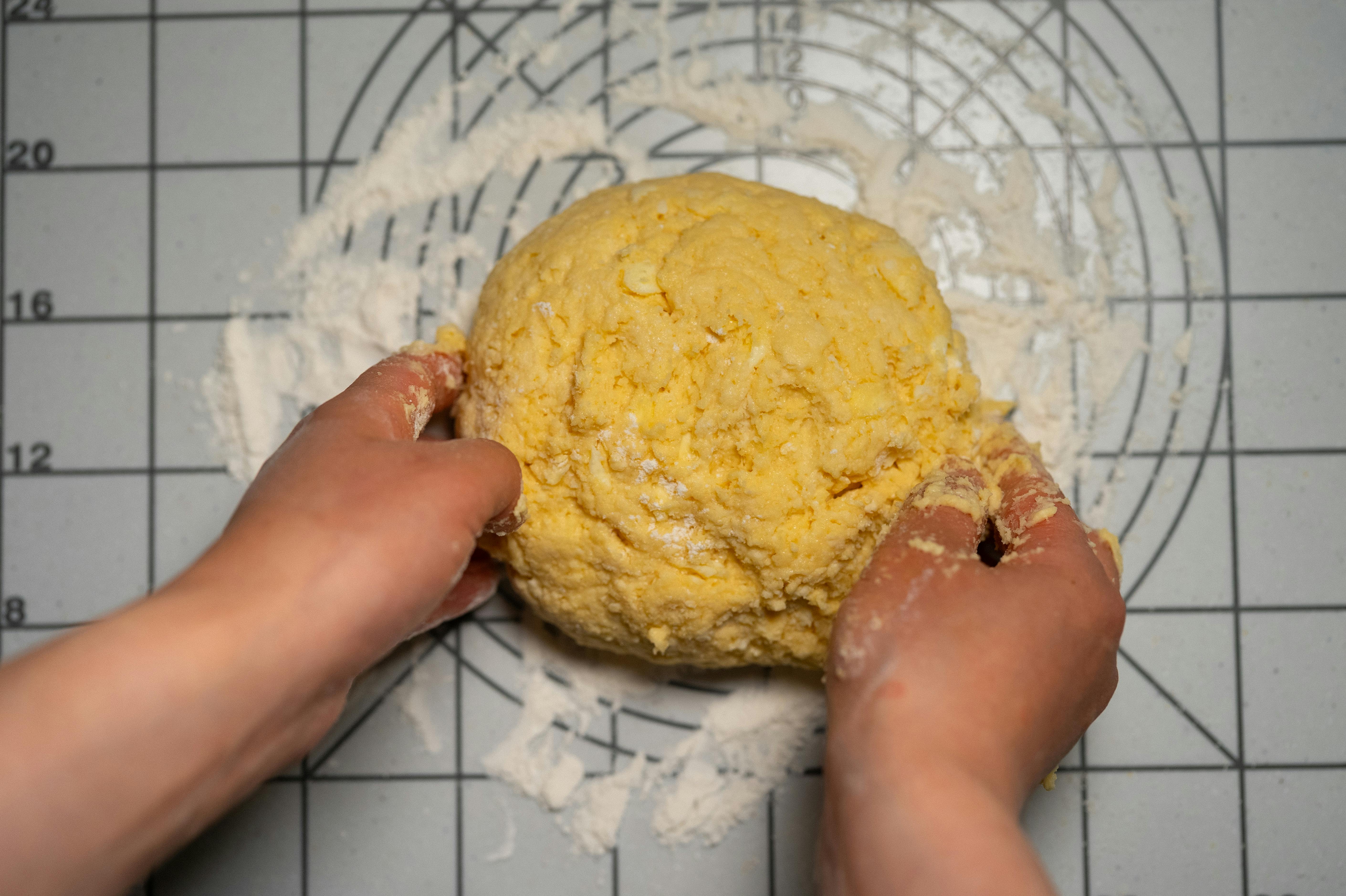 Close-up of hands kneading homemade pasta dough on a floured work surface.