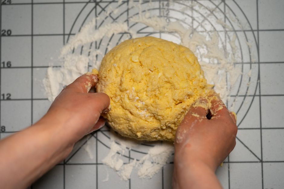 Close-up of hands kneading homemade pasta dough on a floured work surface.