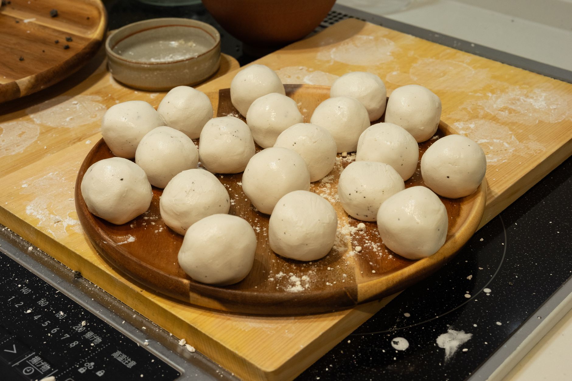 Round dough balls on a wooden plate, ready for baking in a cozy kitchen setting.