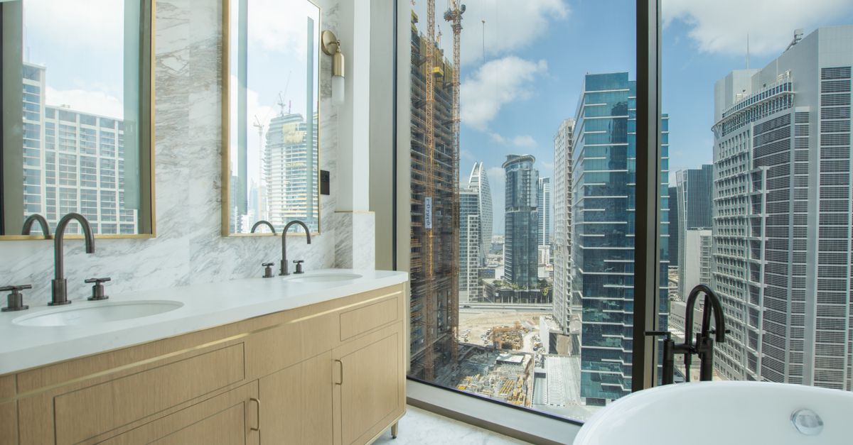 A modern bathroom interior with marble finishes and a stunning view of a city skyline through large windows.