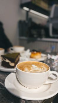 Close-up of a latte art coffee with desserts in a cozy cafe setting.