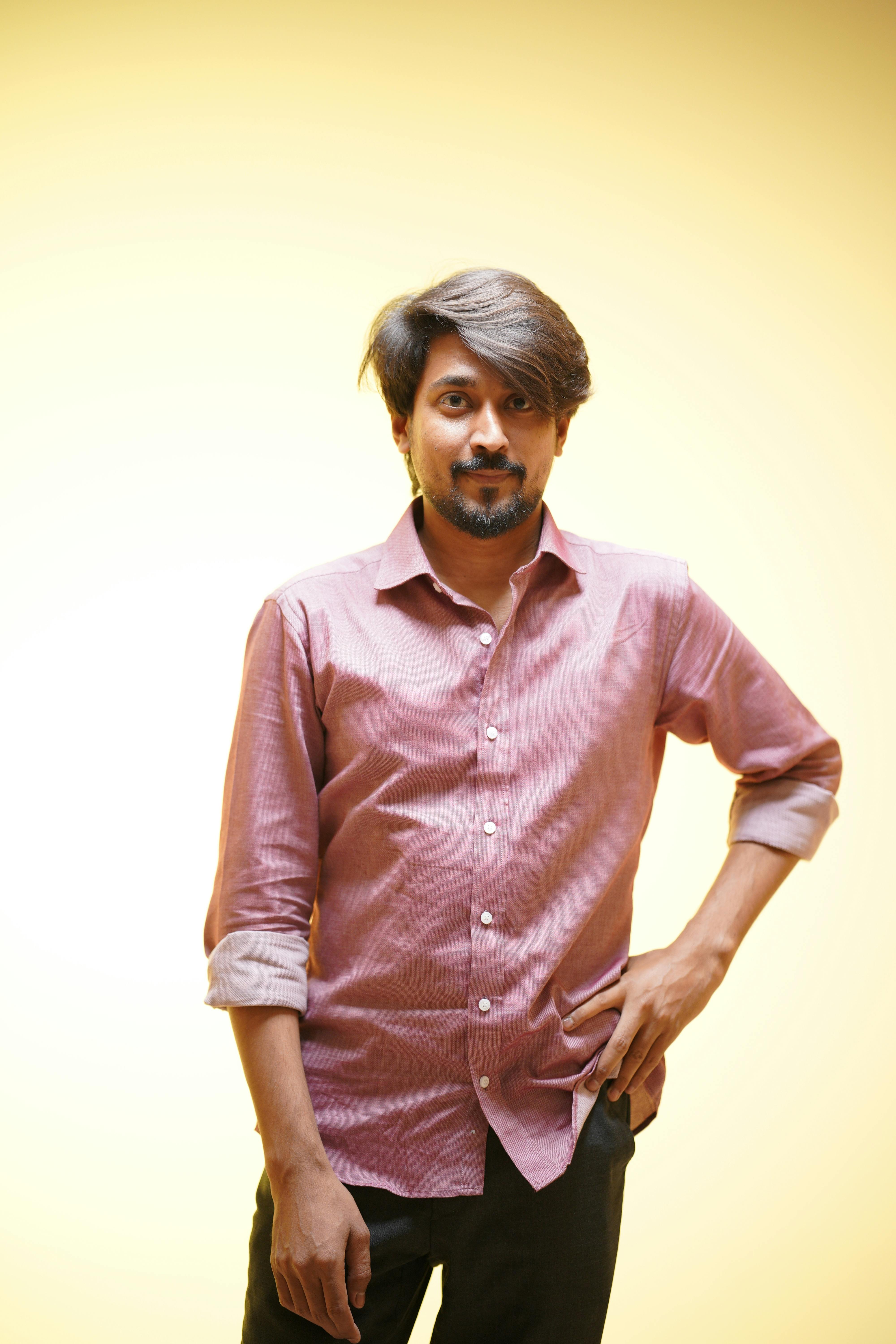 Portrait of a confident man wearing a pink shirt against a yellow background.