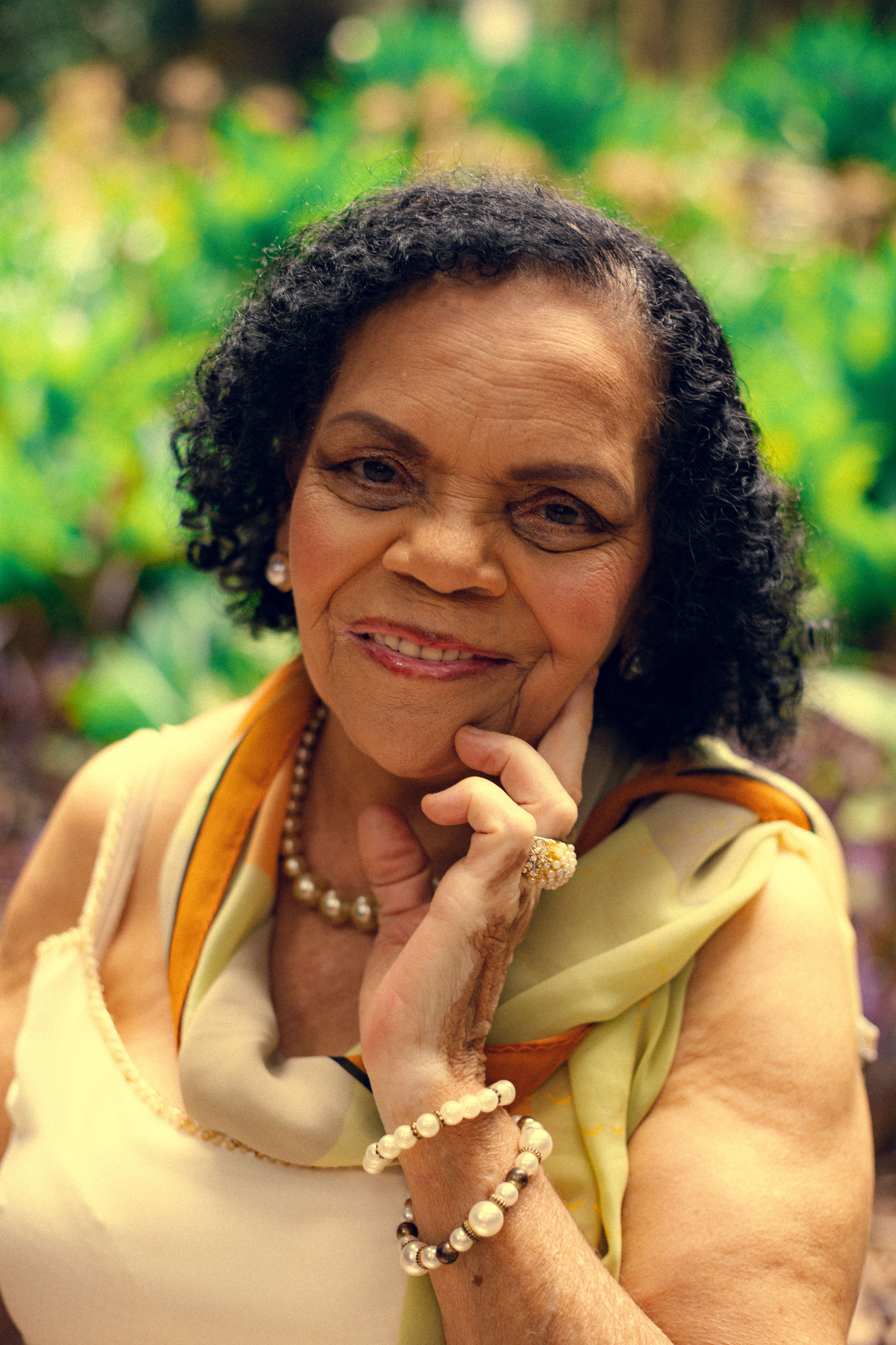 Portrait of a senior woman with pearls, smiling warmly in an outdoor setting in São Paulo.