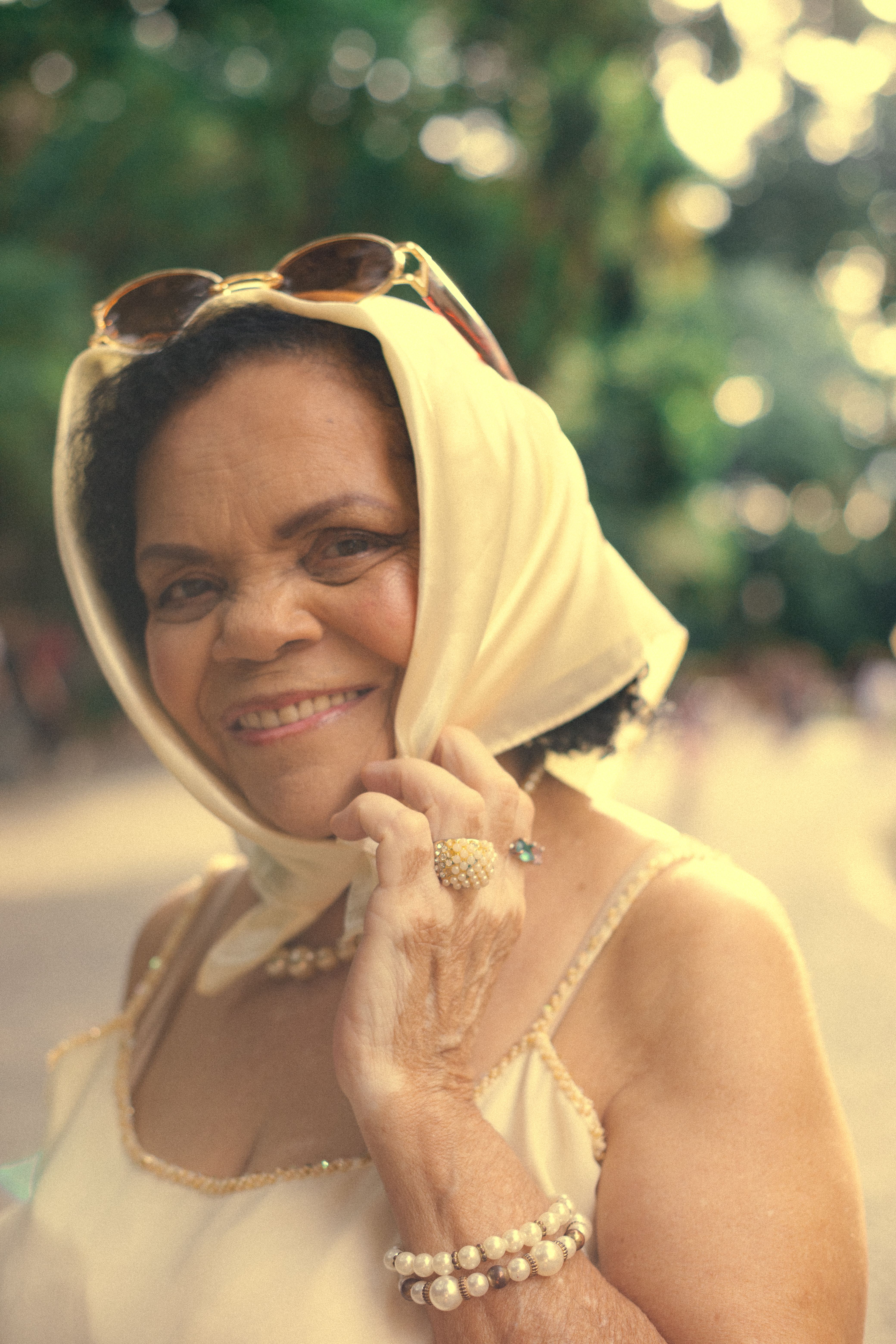 A senior woman smiling outdoors in a vintage style, with greenery in São Paulo.