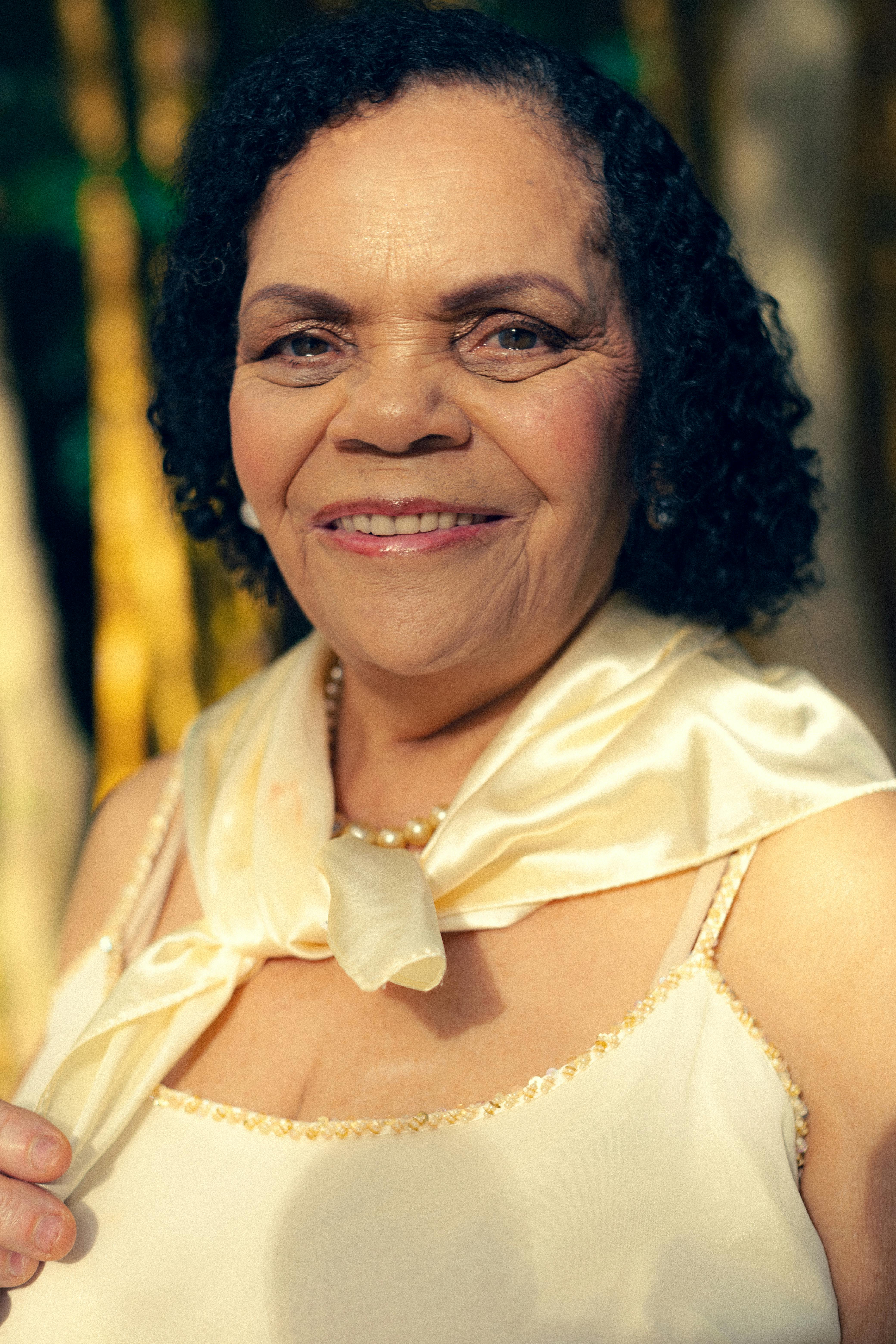 Elegant portrait of a senior woman smiling warmly in an outdoor setting.