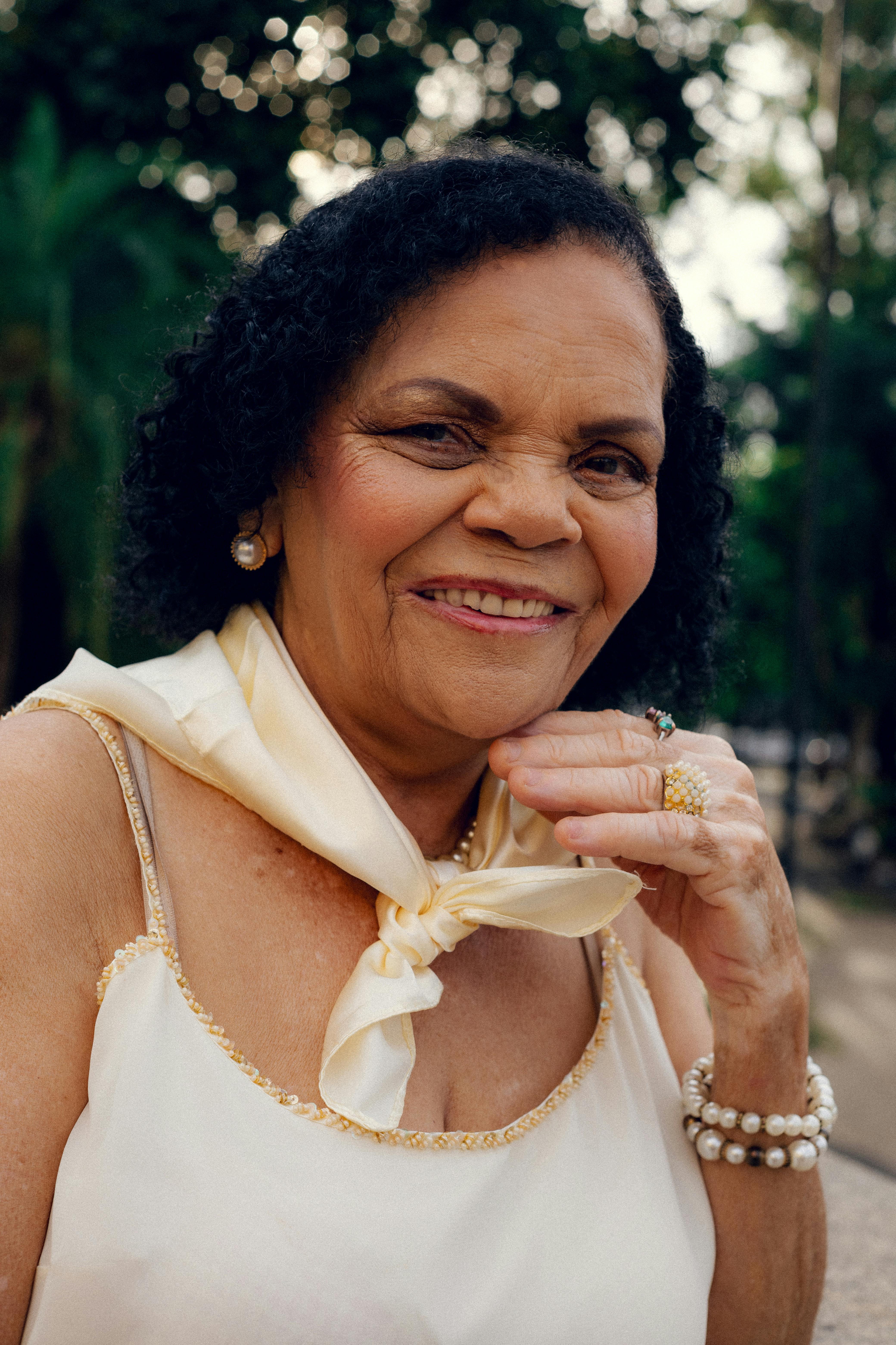 Charming senior woman in a white dress with accessories smiling outdoors in São Paulo.