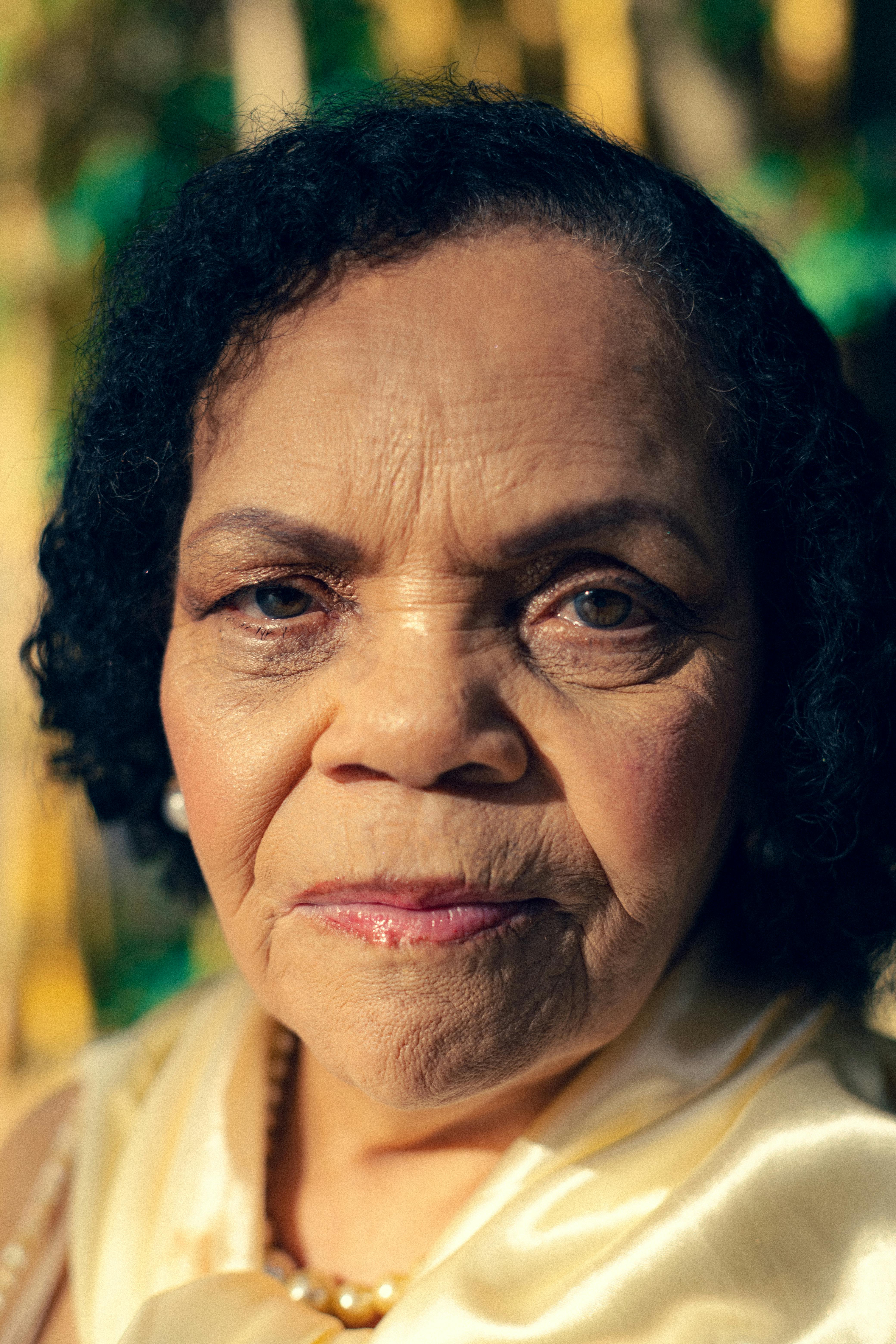 Close-up portrait of a senior woman in sunlight, wearing pearl earrings.