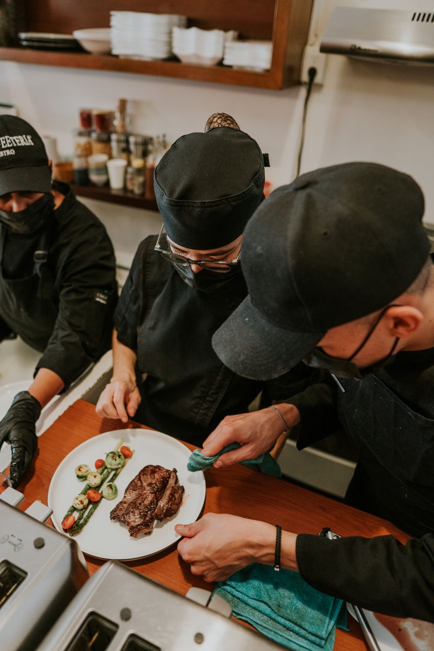 Team of chefs focused on plating a gourmet steak dish in a professional kitchen setting.