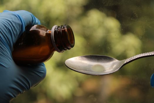 Close-up of medicine being poured into a spoon with a green outdoor background.