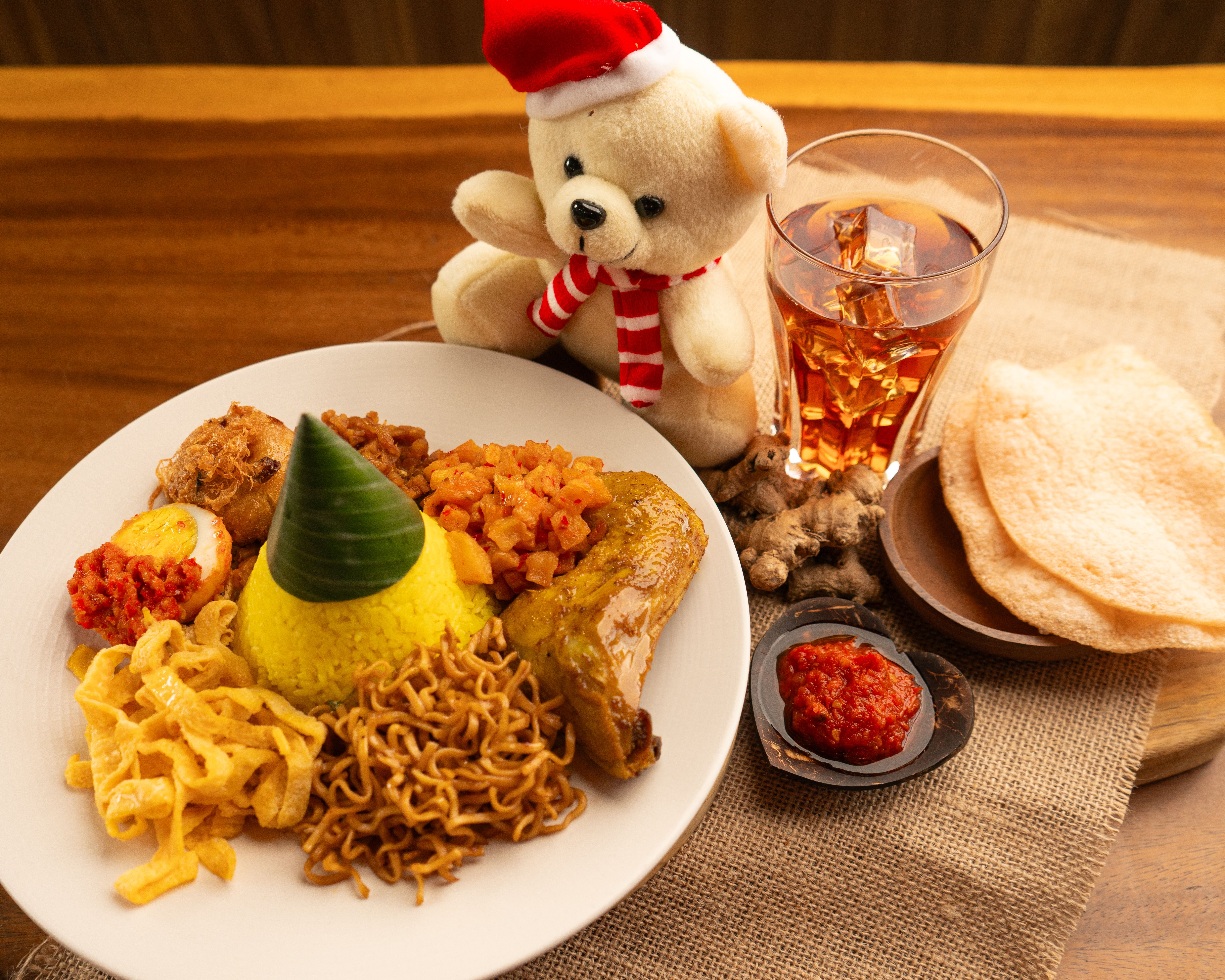 Asian dish with festive elements, toy bear in Santa hat, and iced drink.