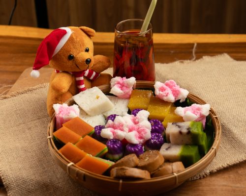 Free A teddy bear in Santa hat next to a tray of colorful sweets and a glass of tea, creating a festive ambiance. Stock Photo