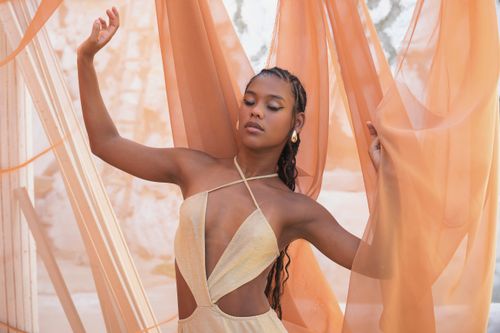 Free Beautiful portrait of a woman posing gracefully among peach-colored sheer fabric outdoors. Stock Photo