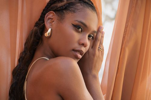 Free Close-up portrait of a woman posing gracefully near peach-colored curtains. Stock Photo