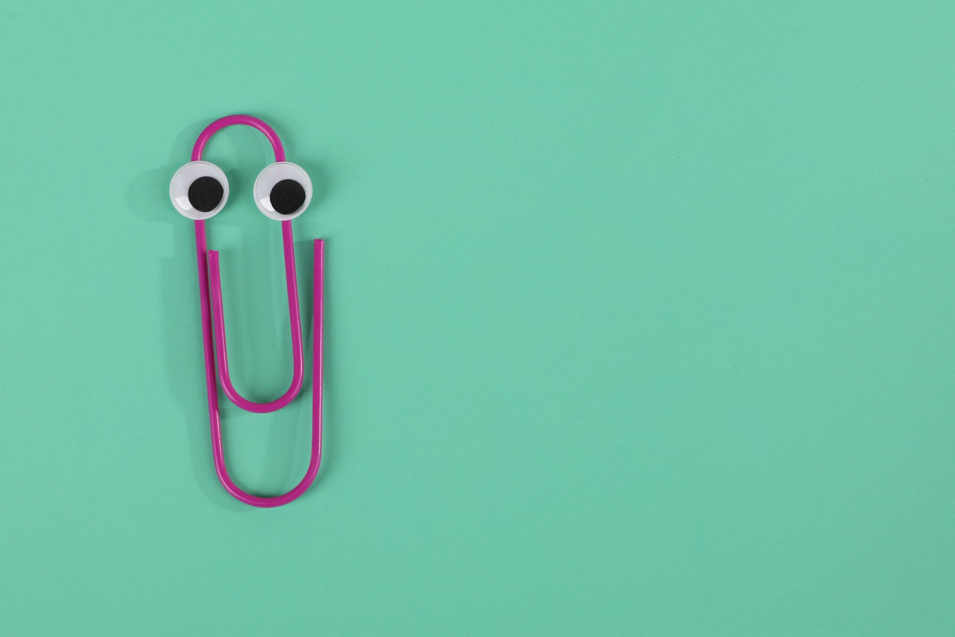 A playful pink paperclip with googly eyes on a green pastel background offers fun visual appeal.