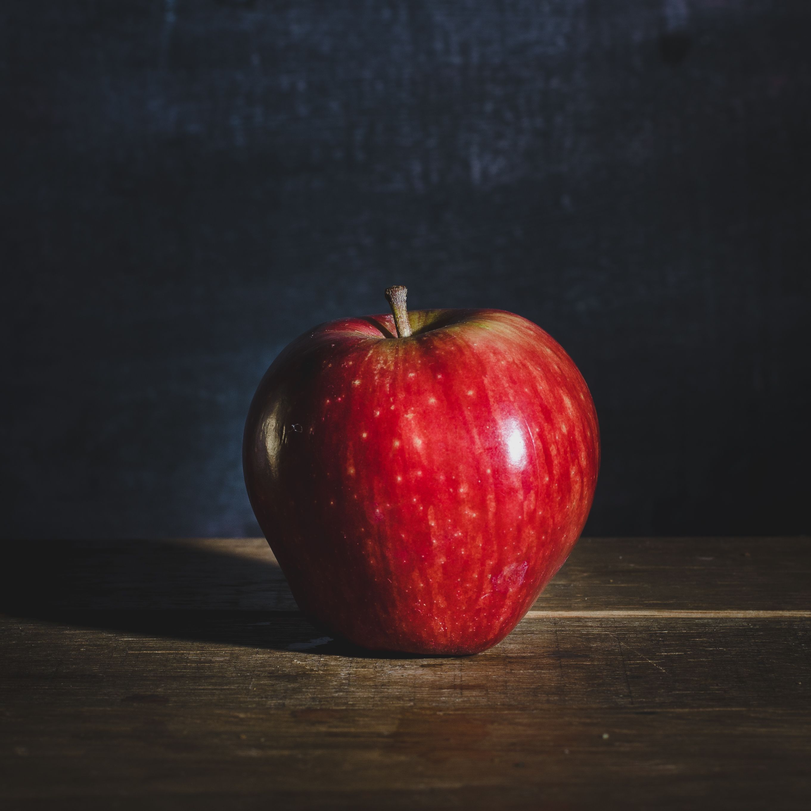 High-quality image of a vibrant red apple placed on a rustic wooden table with a dark backdrop.
