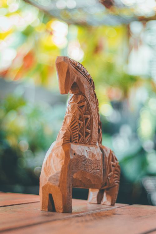 Free A beautifully crafted carved wooden horse sculpture with detailed patterns stands against a colorful blurred background. Stock Photo