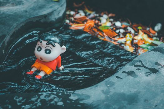 Toy figure of animated character in a dark water stream surrounded by fallen leaves.